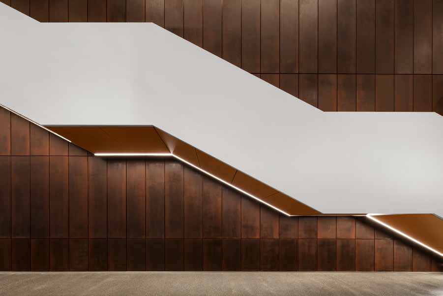 A folded white stair cantilevered across a wall of deep brown timber panels, a thin line of light tracing the full length of its underside.